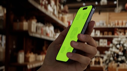 GREEN SCREEN CHROMA KEY Hand holding a phone in a Christmas decor shop, surrounded by festive lights and decorations