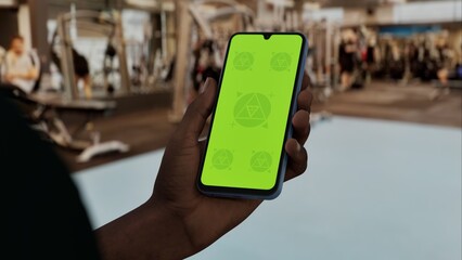 GREEN SCREEN CHROMA KEY A hand holding a phone with a green screen at a gym background filled with fitness equipment and active people exercising