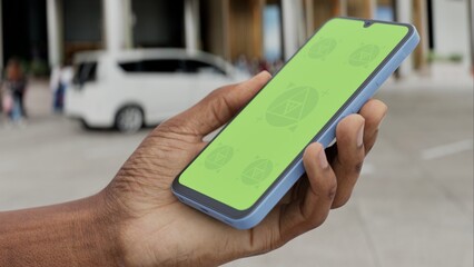 GREEN SCREEN CHROMA KEY Smartphone with a green screen held in a hand near a hotel entrance, featuring a parked car and modern urban surroundings