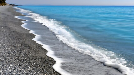 Obraz premium Tranquil Rocky Beach with Gentle Waves Lapping Against the Shore Under Clear Blue Sky