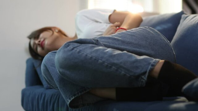 Young woman is experiencing intense abdominal pain. She is writhing in discomfort on a sofa.