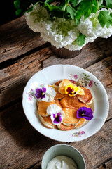 pancakes with edible flowers. Wooden background, top view.