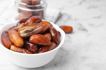 Tasty dried dates in bowl and jar on white marble table, closeup. Space for text