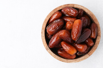 Tasty dried dates in wooden bowl on white table, top view. Space for text