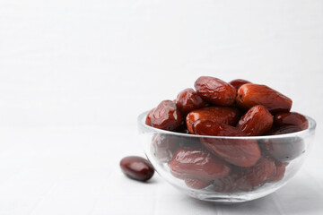 Tasty dried dates in glass bowl on white table, closeup. Space for text