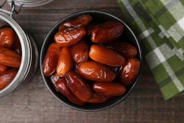 Tasty dried dates in bowl and jar on wooden table, flat lay