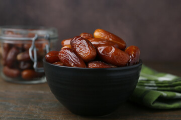 Tasty dried dates in bowl and jar on wooden table, closeup