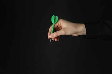Woman holding dart on black background, closeup. Space for text