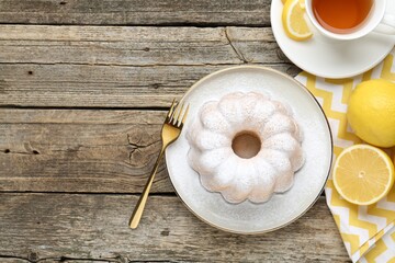 Tasty lemon cake with powdered sugar, fresh fruits and tea on wooden table, flat lay. Space for text