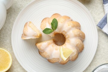 Delicious lemon cake with glaze and mint on light textured table, flat lay