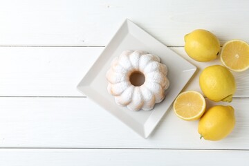 Delicious lemon cake with powdered sugar and citrus fruits on white wooden table, flat lay. Space...