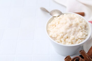 Tasty rice pudding with cinnamon served on white tiled table, closeup. Space for text