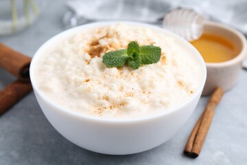 Tasty rice pudding with cinnamon, mint and honey on light grey table, closeup