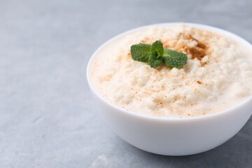 Tasty rice pudding with cinnamon and mint in bowl on grey table, closeup. Space for text
