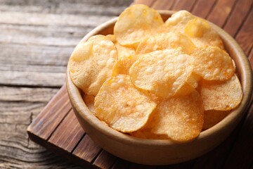 Tasty potato chips in bowl on wooden table, closeup