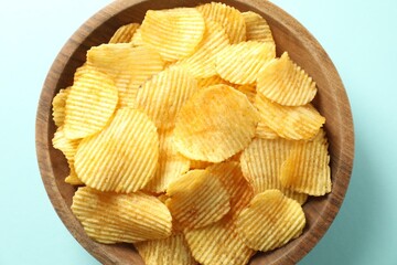 Tasty potato chips in bowl on light blue background, top view