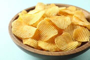 Tasty potato chips in bowl on light blue background, closeup