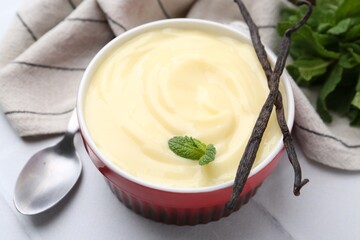 Tasty vanilla pudding, mint and pods on white tiled table, closeup