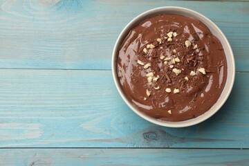 Tasty chocolate pudding in bowl on light blue wooden table, top view. Space for text