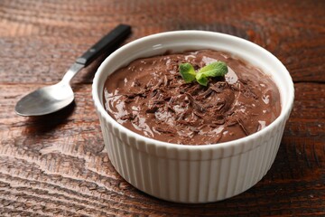 Tasty chocolate pudding in bowl and spoon on wooden table, closeup