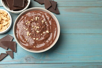 Tasty chocolate pudding in bowl and ingredients on light blue wooden table, flat lay. Space for text