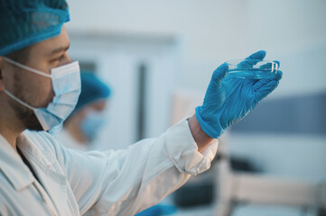 team of doctors man and woman in protective medical clothing with petri dish and flask conducting...