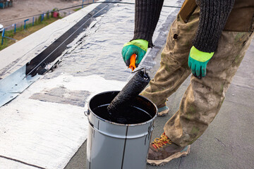 a young worker treats a roof with bitumen primer before applying rolled asphalt roofing using a torch