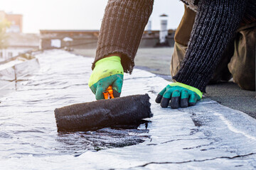 a young worker treats a roof with bitumen primer before applying rolled asphalt roofing using a torch