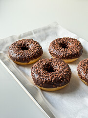 Brown chocolate donuts on metal tray and white table top view