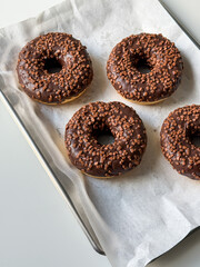 Brown chocolate donuts on metal tray and white table top view