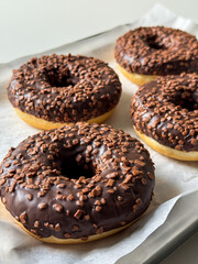 Brown chocolate donuts on metal tray and white table close up