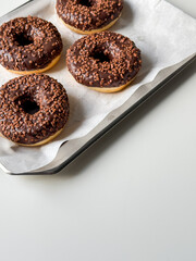 Brown chocolate donuts on metal tray and white table top view with copy space