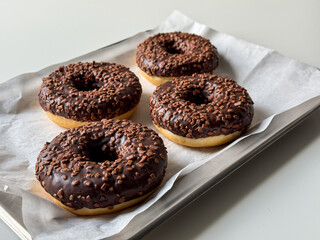 Brown chocolate donuts on metal tray and white table side view