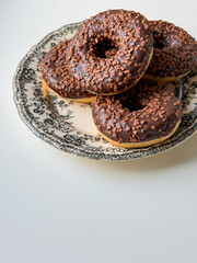 Brown chocolate donuts on plate with floral print and white table with copy space