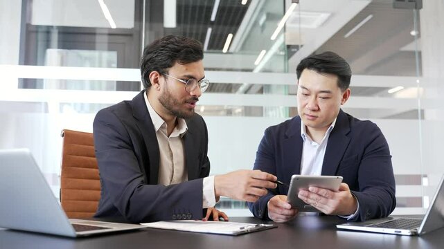 Two businessmen discussing business strategy at a meeting in modern office with digital tablet. Colleagues collaborate, discuss details while reviewing documents. talking about the development project