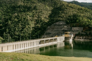 Fototapeta premium Dam with forested hillside and calm reservoir.