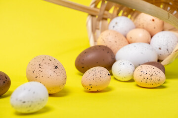 aesthetic easter composition with speckled eggs spilling from wicker basket onto vibrant yellow background