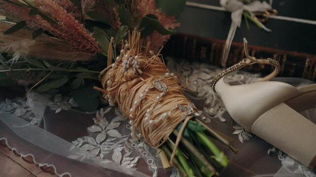 Close up of a rustic wedding bouquet wrapped in raffia with pearls, next to bridal heels