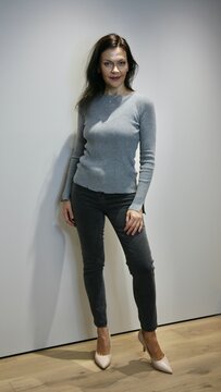 Positive woman 51 years old with evening make-up in a grey sweater and jeans in pink high-heeled shoes posing and looking at the camera
