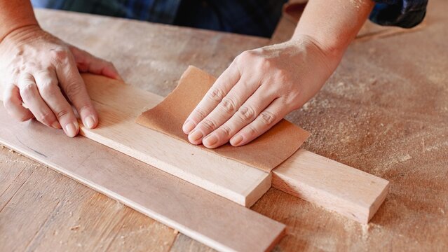 Close-up of hands sanding wood. Woodworking of sanding, smoothing, and crafting. Hands focus on sanding a smooth wood surface. Craftsmanship in action. Woodworking and construction work concept.
