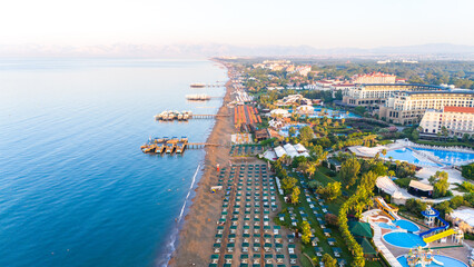 Fototapeta premium Aerial view of a luxurious beachfront resort with private piers, pools, and sunbeds along the coastline