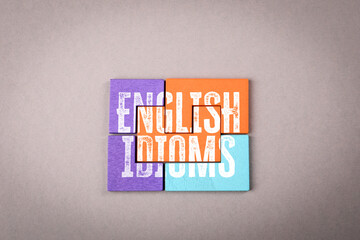 English Idioms. Colorful wooden puzzle pieces on a gray background