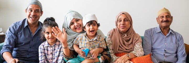 A muslim family of six, including men, women, and children, sitting together. They are smiling, showing a sense of unity and happiness. Muslim family sitting together on sofa.