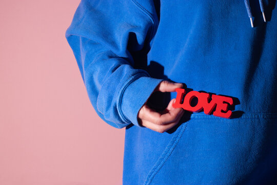 Hand holding red text Love against blue sweatshirt backdrop