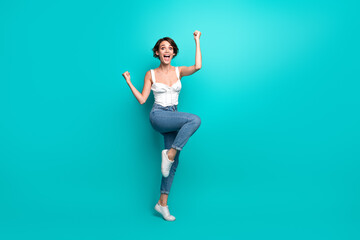 Cheerful young woman in a casual outfit expressing happiness on a vibrant teal background,...