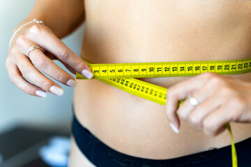 Woman measuring her waist with yellow measuring tape for weight loss progress