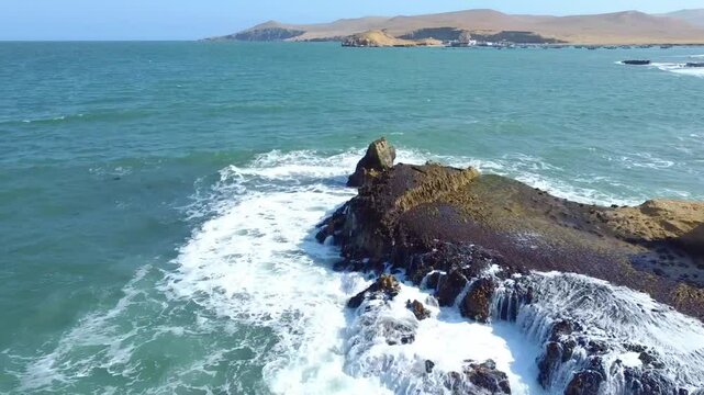 Drone footage of a Paracas National Reserve and waves clashing rocks on a sunny day