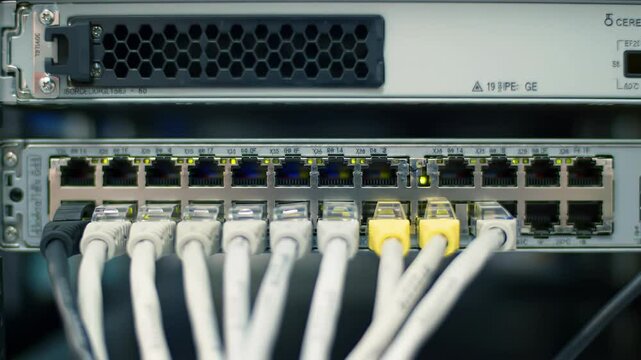 Network switch with ethernet cables connected in server rack, multiple ports with white and yellow patch cords plugged in, technology infrastructure for data communication and internet connectivity