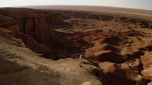 A girl walking through the Mars-like hills of Tsagaan Suvarga, Mongolia, captured in breathtaking aerial drone footage at sunset.
