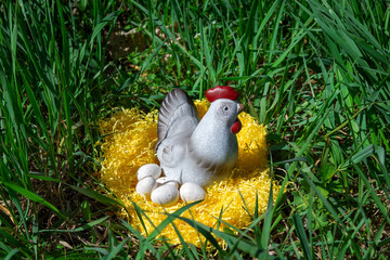 Decorative ceramic hen with speckled eggs on yellow straw in green grass. Spring and Easter symbol.